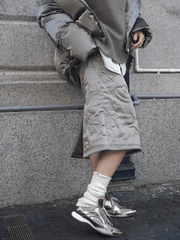 Person wearing a quilted beige coat and silver sneakers against a gray background.