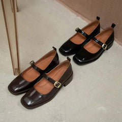 Pair of black and brown shoes with buckles on a light gray floor.