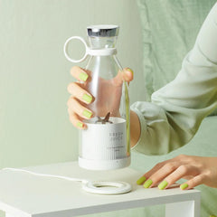 Person holding a glass carafe with a white base labeled 'Fresh Juice' on a light green background.