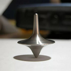A silver-colored metal spinning top gyro, displayed on a flat surface, with a blurred background suggesting motion or spinning.