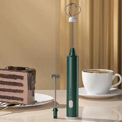 Green handheld milk frother with a cake and coffee cup on a beige background