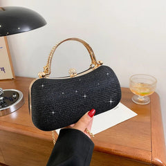 Black handbag with gold handle held by a hand on a wooden surface.
