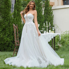 Woman in a white wedding dress standing outdoors with greenery and a table in the background.