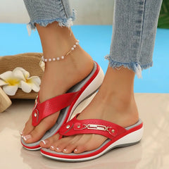 Red sandals with white soles worn by a person on a beach setting
