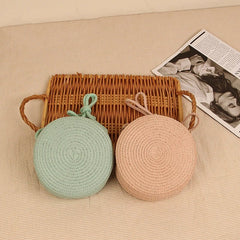 Two round woven bags, one green and one pink, placed on a textured surface with a wicker basket and magazine in the background.