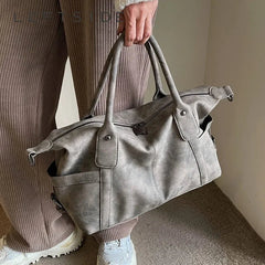 Person holding a gray leather duffel bag with a neutral background