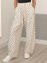 Person wearing white pants with black polka dots and white sneakers in a minimal indoor setting.
