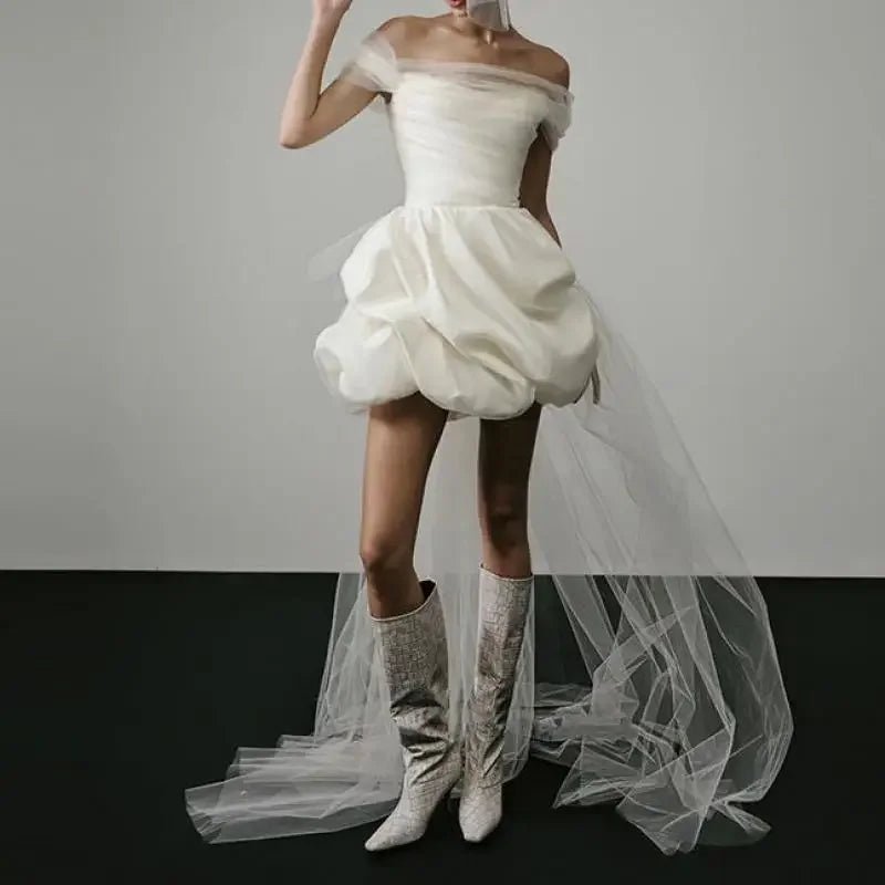 White off-shoulder dress with ruffled skirt and white knee-high boots on a plain background