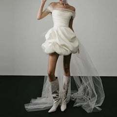 White off-shoulder dress with ruffled skirt and white knee-high boots on a plain background
