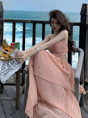 Woman in a peach dress sitting on a wooden deck by the ocean, holding a glass.