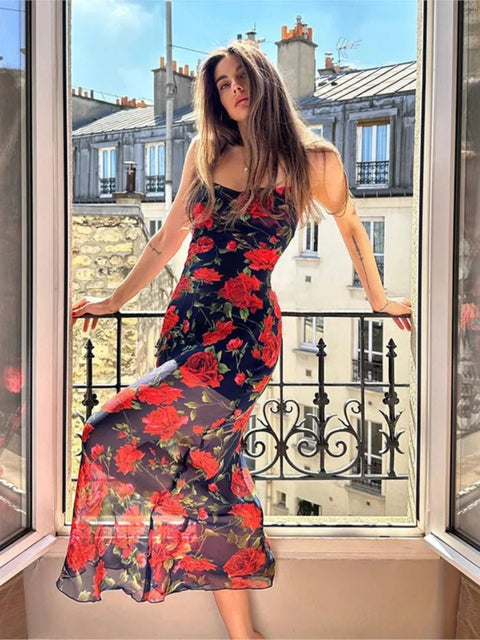 Woman in a floral dress standing on a balcony with a cityscape view.