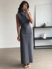 Woman wearing a gray sleeveless dress taking a mirror selfie in a minimalistic room.