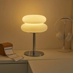 Modern table lamp with a warm glow on a desk next to a book and headphones.