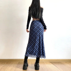 Person wearing a blue plaid skirt and black platform boots against a white wall.