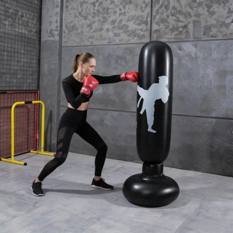 Woman practicing boxing on an inflatable punching bag in a gym setting.