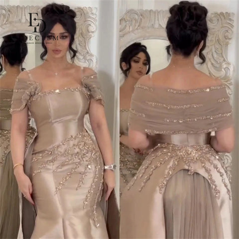 Woman in a beige evening gown with intricate detailing, standing in front of a decorative mirror.