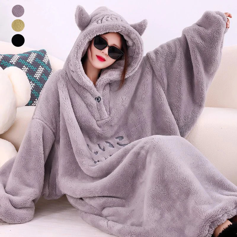 A person wearing a gray fleece oversized blanket robe with a hood, posing on a cozy surface.
