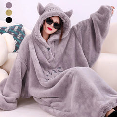 A person wearing a gray fleece oversized blanket robe with a hood, posing on a cozy surface.
