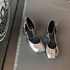Silver high-heeled shoes on a gray surface with a patterned wall in the background