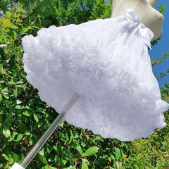 White fluffy parasol held by a mannequin against a green leafy background