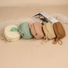 Five woven bags in different colors arranged on a textured surface with a magazine underneath.