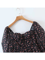 Black floral dress on a wooden hanger against a white background