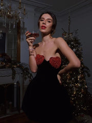 Woman in a black dress with red heart details holding a glass in an elegant room.