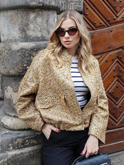 Woman wearing a gold sequin jacket and sunglasses against a stone wall.