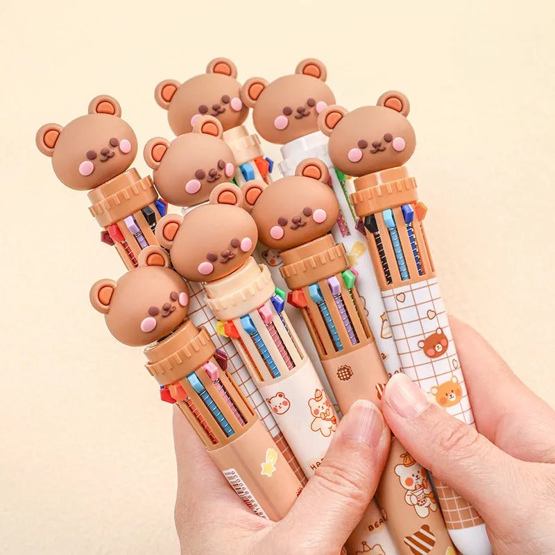Set of colorful pens with bear-shaped caps held by a hand on a beige background