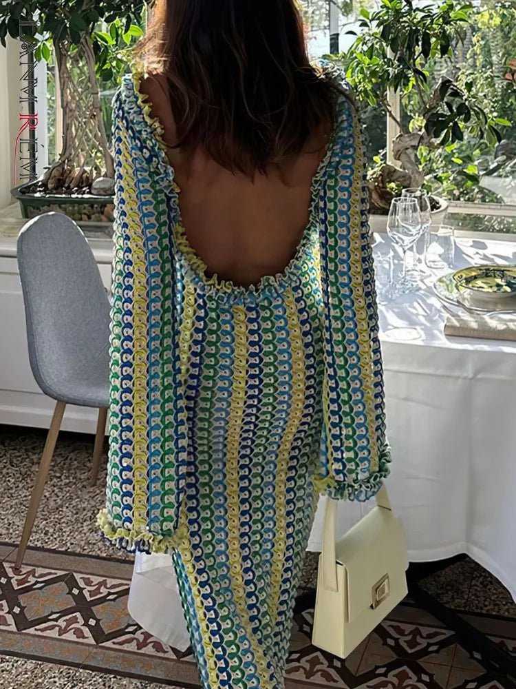 Woman in a patterned dress with a backless design, standing in a room with plants and a table.