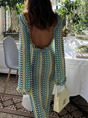 Woman in a patterned dress with a backless design, standing in a room with plants and a table.