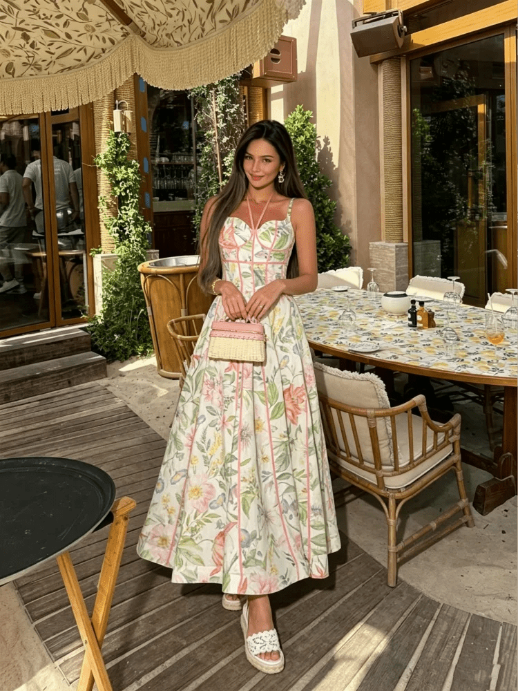 Woman in a floral dress standing in an outdoor setting with tables and chairs.