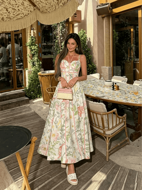 Woman in a floral dress standing in an outdoor setting with tables and chairs.