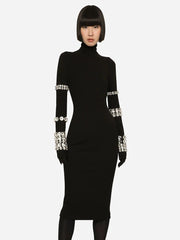 Black dress with silver embellishments on sleeves and cuffs worn by a model against a white background