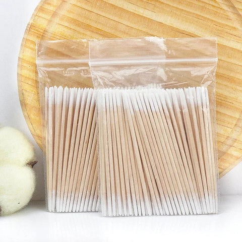 Packaged wooden toothpicks on a white surface with a wooden plate in the background.