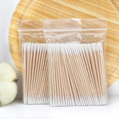 Packaged wooden toothpicks on a white surface with a wooden plate in the background.