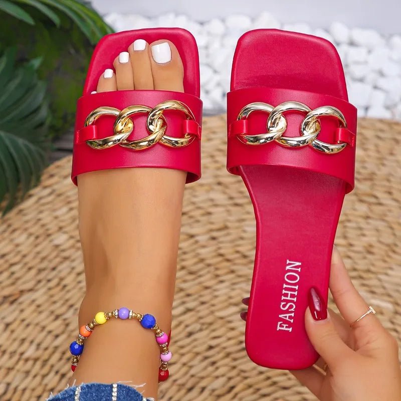 Red sandals with gold chain detail worn by a person on a woven surface.