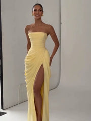 Woman wearing a yellow strapless gown with a high slit on a plain background