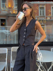 Woman in a dark outfit drinking from a paper cup in an outdoor cafe setting.