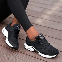 Black athletic shoes with white soles worn by a person on a wooden floor.