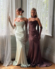 Two women in elegant evening gowns standing in a room with large windows.