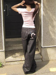 Person wearing a pink shirt and dark jeans with heart designs, standing against a building.