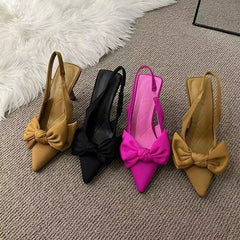 Four high-heeled shoes with bow details on a textured surface.