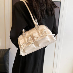Person holding a gold handbag with a bow detail against a neutral background