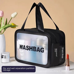 Black washbag with clear front panel displaying skincare products, surrounded by flowers and makeup items on a beige background.