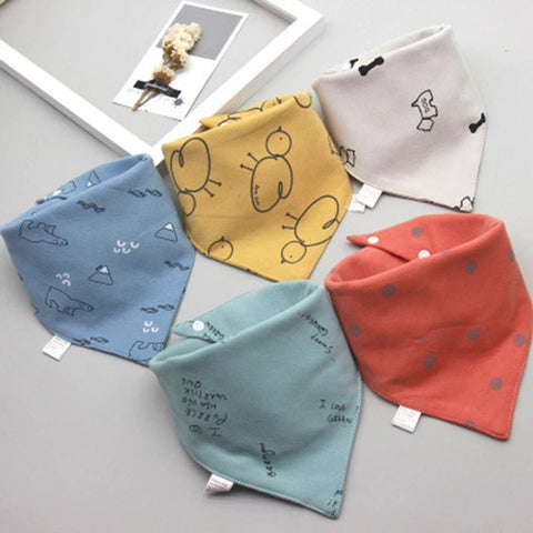 Five colorful baby bibs with different patterns on a light gray surface.