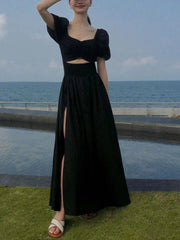 Person wearing a black dress with a cutout design by the ocean.