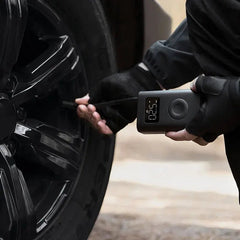 Person checking tire pressure with a digital gauge on a car tire.