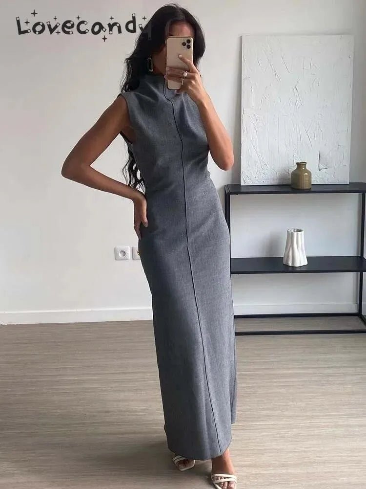 Woman wearing a gray sleeveless dress taking a mirror selfie in a minimalistic room.