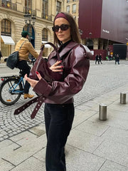 Woman in a maroon leather jacket holding a matching bag on a city street.